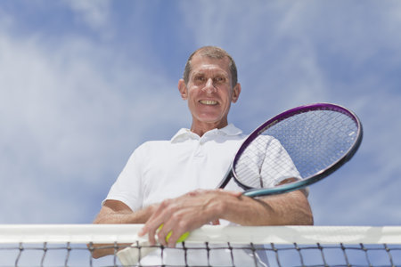 Older man leaning on tennis netの写真素材