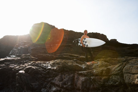 Man holding surfboard on large rocks.の写真素材