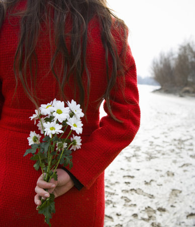 Young woman holding flowers behind back, rear, mid-sectionの写真素材