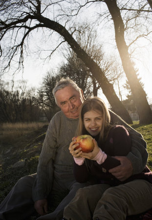 Grandfather and granddaughter (10-12) sitting outdoors, smilingの写真素材