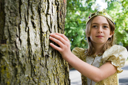Girl dressed up as queen touching tree trunkの写真素材