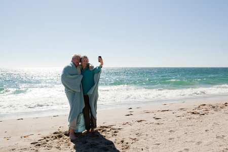 Couple at the beach in blanket, photographing themselvesの写真素材