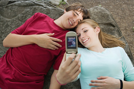 Teenage couple using a camera telephoneの写真素材