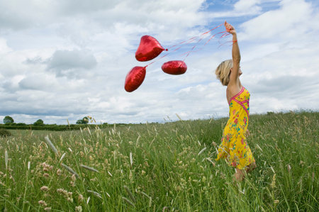 Woman walking with balloons in fieldの写真素材