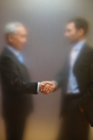 Men shaking hands behind frosted screenの写真素材