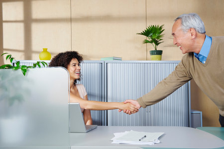 Man and woman shaking hands at deskの写真素材