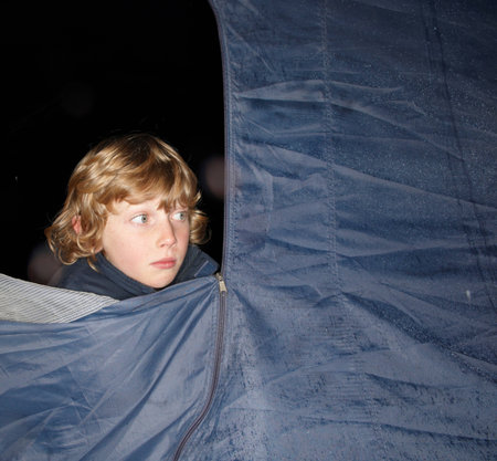 Boy looking out of tent at duskの写真素材