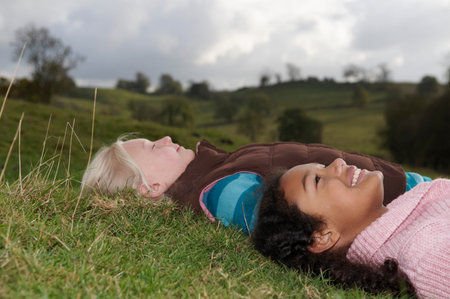 Two girls lying on grass looking at skyの写真素材