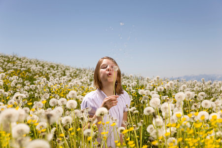 Girl in meadow blowing dandelion seeds