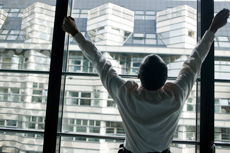 man at window with raised armsの写真素材