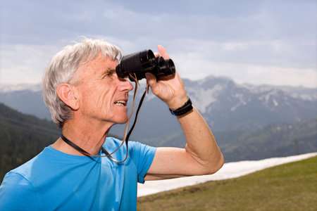 senior man with binoculars in mountainsの写真素材