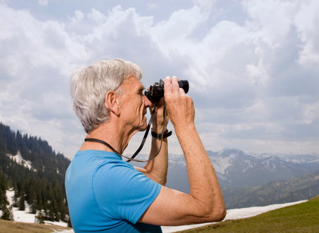 senior man with binoculars in mountainsの写真素材