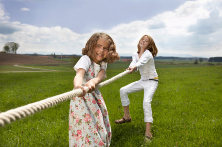 Children pulling a rope in countrysideの写真素材