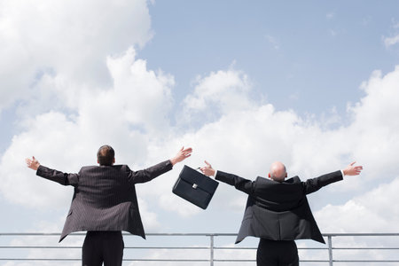 two business men throwing arms in skyの写真素材