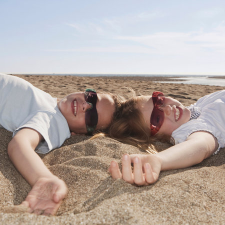 Children with sunglasses laying on sandの写真素材