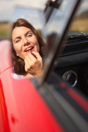 Woman applying lipstick in cars mirrorの写真素材