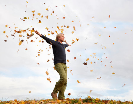 man walking through flying autumn leavesの写真素材