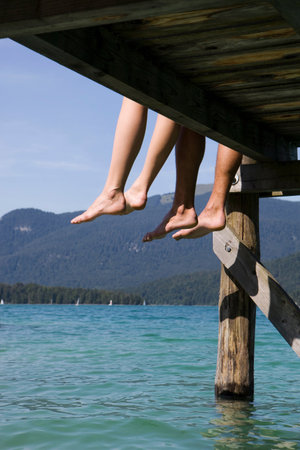 Two people sitting barefoot by a lakeの写真素材