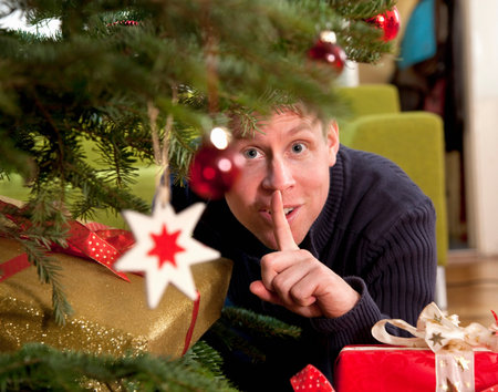 man hiding presents under christmas treeの写真素材