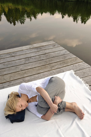 Young woman lying on blanket by lakeの写真素材