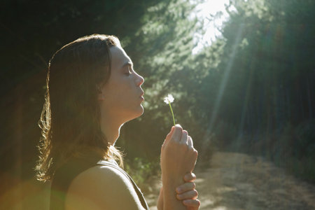 Young man blowing dandelion in forestの写真素材
