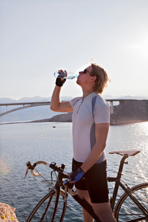 Cyclist drinking water by seaの写真素材