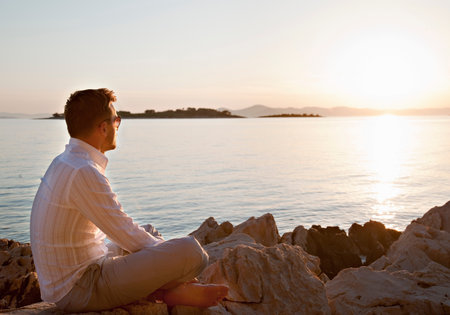Man watching sun set at rocky beachの写真素材