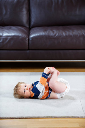 8 month old baby in diaper lying on rugの写真素材