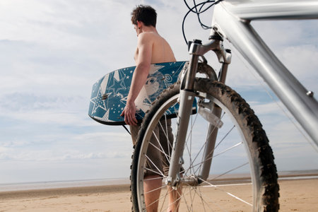 Man on beach with bike and boogie boardの写真素材