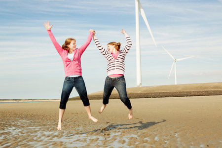 Two girls jumping on beach with turbinesの写真素材