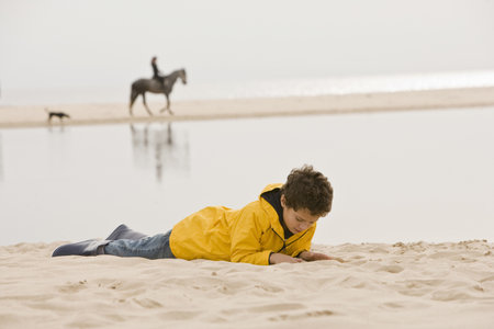 Young boy lying on sand at beachの写真素材