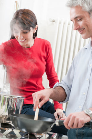 Happy couple cooking together at kitchenの写真素材