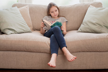 young girl reading book on sofaの写真素材
