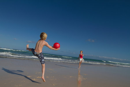 Children playing with red ball on beachの写真素材