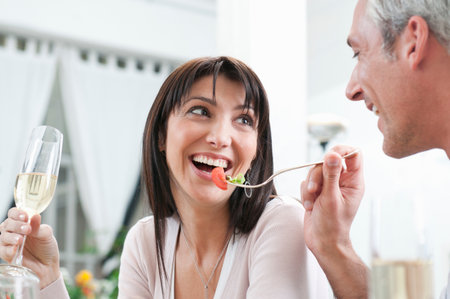 Happy couple feeding together at lunchの写真素材