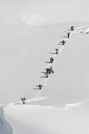 Snowboarders walking up mountainsideの写真素材