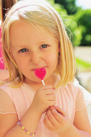 Girl eating heart-shaped lollipopの写真素材