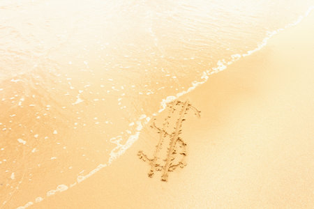 Dollar sign in sand washed away by wavesの写真素材