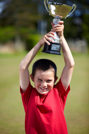 Boy cheering with trophy outdoorsの写真素材