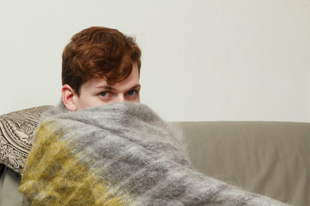 Man wrapped in blanket on couchの写真素材