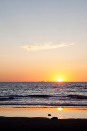 Sun setting over ocean on beachの写真素材