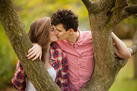 Teenage couple kissing in tree in parkの写真素材