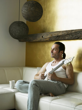 Man playing guitar on couchの写真素材