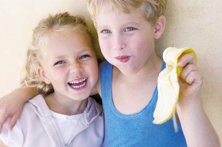 Boy hugging sister and eating bananaの写真素材