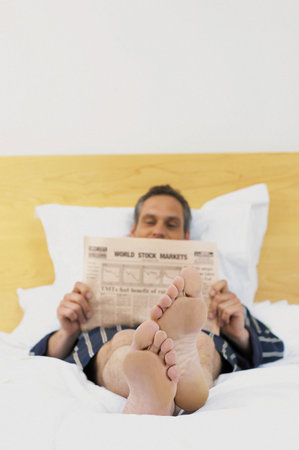 Man reading newspaper in bedの写真素材