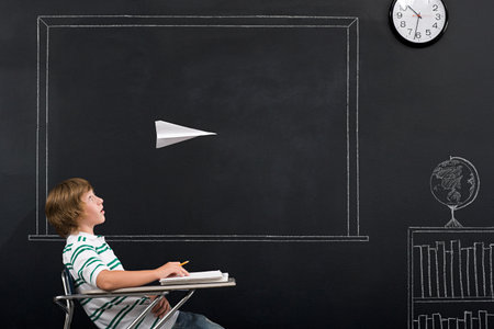 A boy with a paper airplane over his headの写真素材