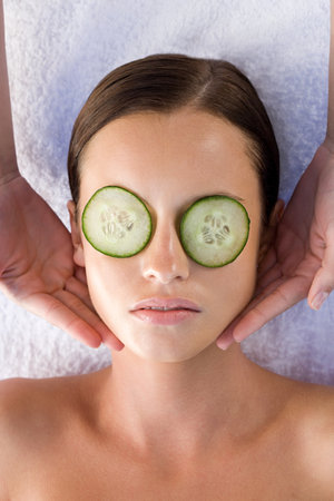 Young woman with cucumber slices over eyes receiving facial massageの写真素材