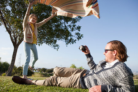 Young man photographing girlfriend as she shakes out a blanketの写真素材