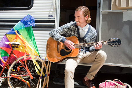 Young man playing guitar by caravan