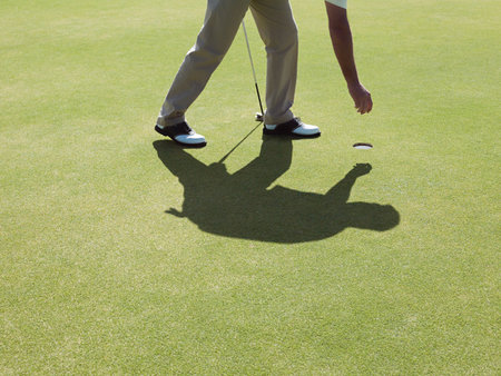 Man playing golf, picking up ballの写真素材